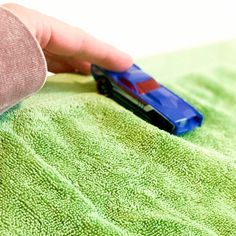 a hand is holding a toy car on a green towel