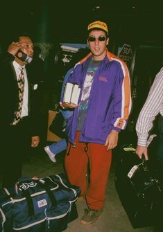 a man standing next to luggage in an airport with two other men looking at the camera