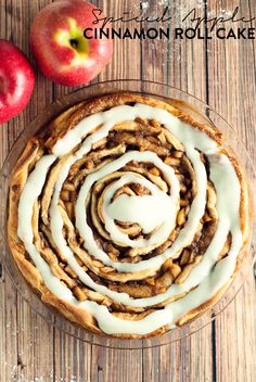 an apple pie with white icing and two apples on the side, sitting on top of a wooden table