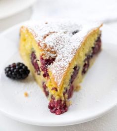 a piece of cake on a white plate with berries and powdered sugar over it