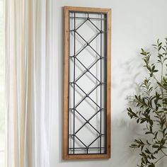 a tall window sitting next to a plant on top of a wooden table in front of a white wall