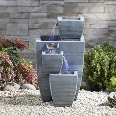 a water fountain is in the middle of some rocks and gravel with plants around it