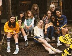 a group of young women sitting next to each other in front of a building with trees