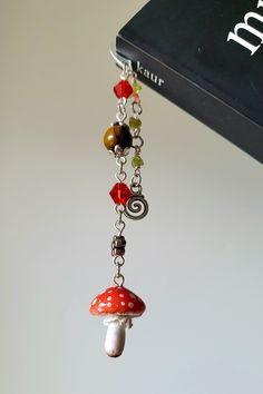 a red mushroom is hanging from a chain with beads and charms on it's end