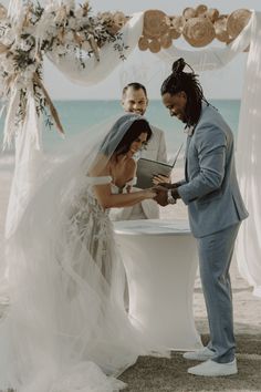 a bride and groom exchanging vows at their wedding ceremony on the beach with an ocean in the background