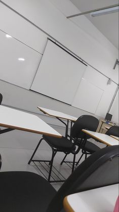 an empty classroom with desks and chairs in front of a whiteboard on the wall