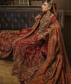 a woman sitting on top of a couch wearing a red and gold wedding dress with an elaborate head piece