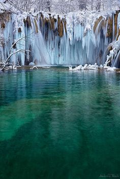 the water is crystal green and blue in this frozen waterfall area, surrounded by snow covered trees