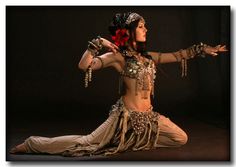 a woman dressed in belly dance clothing and holding her arms out to the side with both hands