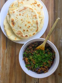 two white bowls filled with food on top of a wooden table next to a tortilla