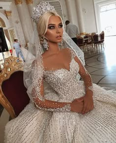 a woman in a white wedding dress sitting on a chair wearing a tiara and veil