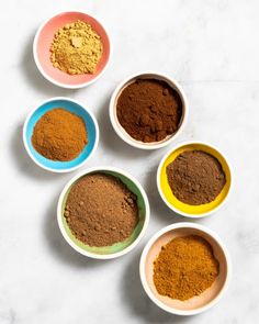 five bowls filled with different colored spices on top of a white countertop next to each other