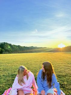 two young women sitting on top of a blanket in the middle of a grass field