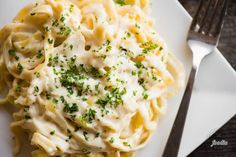 a white plate topped with pasta covered in sauce and parsley next to a fork