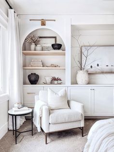 a white chair sitting in front of a book shelf filled with books and vases