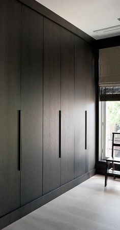 an empty room with wooden cabinets and a bench in the corner, next to a window