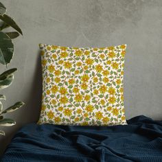 a yellow and green floral pillow sitting on top of a bed next to a potted plant