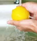 a person holding a lemon in their hand under a faucet with water running from it