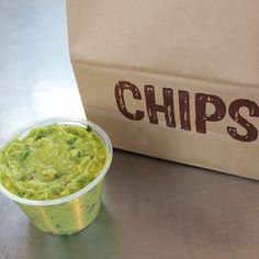 a bowl of guacamole next to a paper bag with the word chips on it