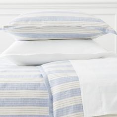 a bed with white and blue striped sheets, pillows and pillow cases on top of it