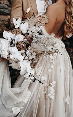 a bride and groom standing next to each other in front of some rocks with flowers