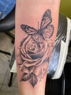 a black and white rose with a butterfly tattoo on it's arm, next to a chair