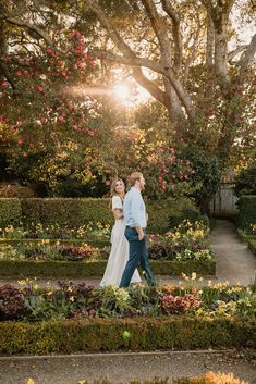 a bride and groom walking through the gardens at sunset