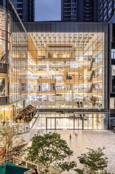 an office building with many windows and people walking in the courtyard area at night time