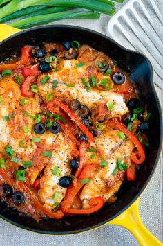 a skillet filled with chicken, peppers and olives on top of a table