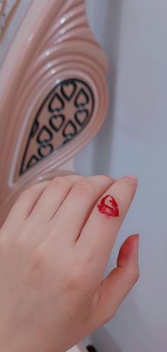 a woman's hand with a red nail polish on her finger and a heart shaped object in the background