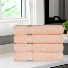 four towels stacked on top of each other in front of a window next to a plant