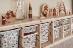 toy storage bins lined up on top of a wooden shelf in a playroom