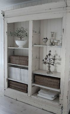 an old white bookcase with wicker baskets and flowers in it is displayed on the wall