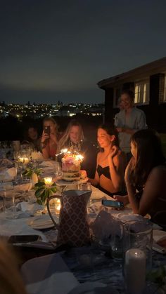 a group of people sitting around a table with a cake and candles in front of them