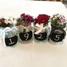 four jars with flowers in them are labeled number twenty five and decorated with ribbons on the table