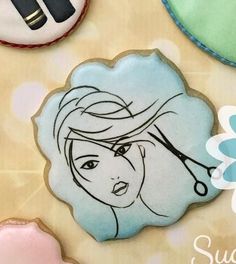 some cookies are decorated to look like women's hair with scissors on them and flowers in the background