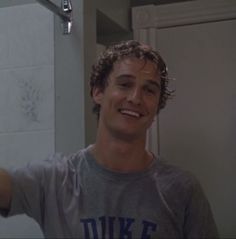 a young man is smiling while brushing his teeth in front of the bathroom mirror,