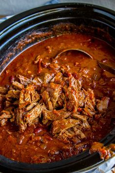 a crock pot filled with shredded meat and tomato sauce on top of a table