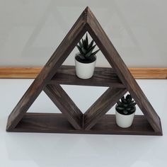 three potted plants are placed in the shape of a triangle on top of a shelf