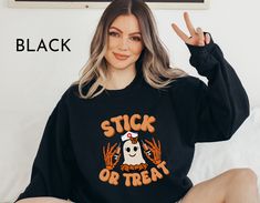 a woman sitting on a bed wearing a black halloween sweatshirt with the words stick or treat printed on it