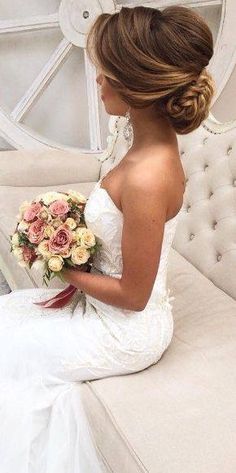 a woman in a wedding dress sitting on a couch holding a bridal bouquet and looking down