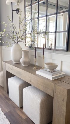 a wooden table topped with white vases next to a mirror