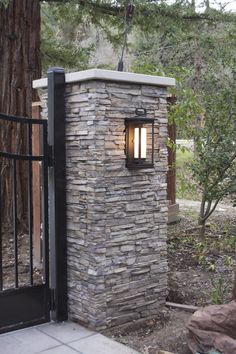 an outdoor light that is on the side of a stone wall in front of a gate