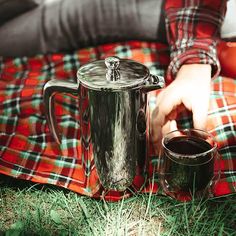 a person is holding a coffee pot and two cups on a blanket in the grass