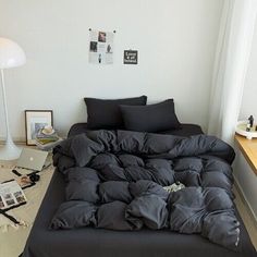 an unmade bed with black sheets and pillows in a white room next to a window