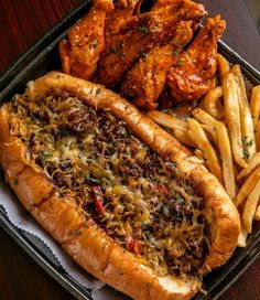 a hot dog and french fries in a tray on a table with some chicken wings