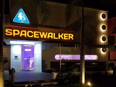 the entrance to spacewalker is lit up at night with palm trees in front