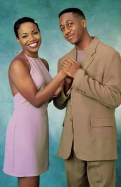 a man and woman standing next to each other in front of a blue background holding hands