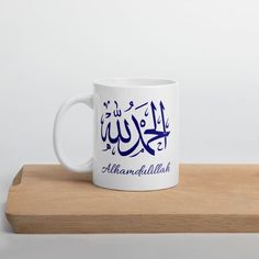 a white coffee mug with arabic writing on it sitting on top of a wooden table