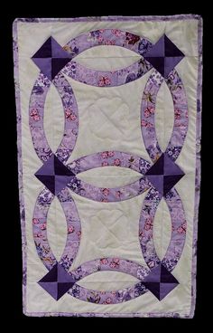 a purple and white quilted wall hanging with circular designs on the front, along with an arrow in the center